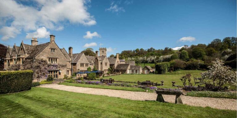 A large stone house with wisteria set amongst green grounds